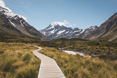 Brown wooden path, surrounded by brown fields, to the mountain
